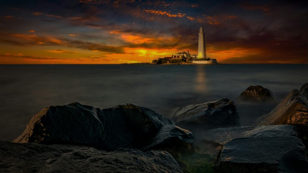 Stunning view of a lighthouse illuminating the rocky shore at sunset, capturing a dramatic seascape vibe.